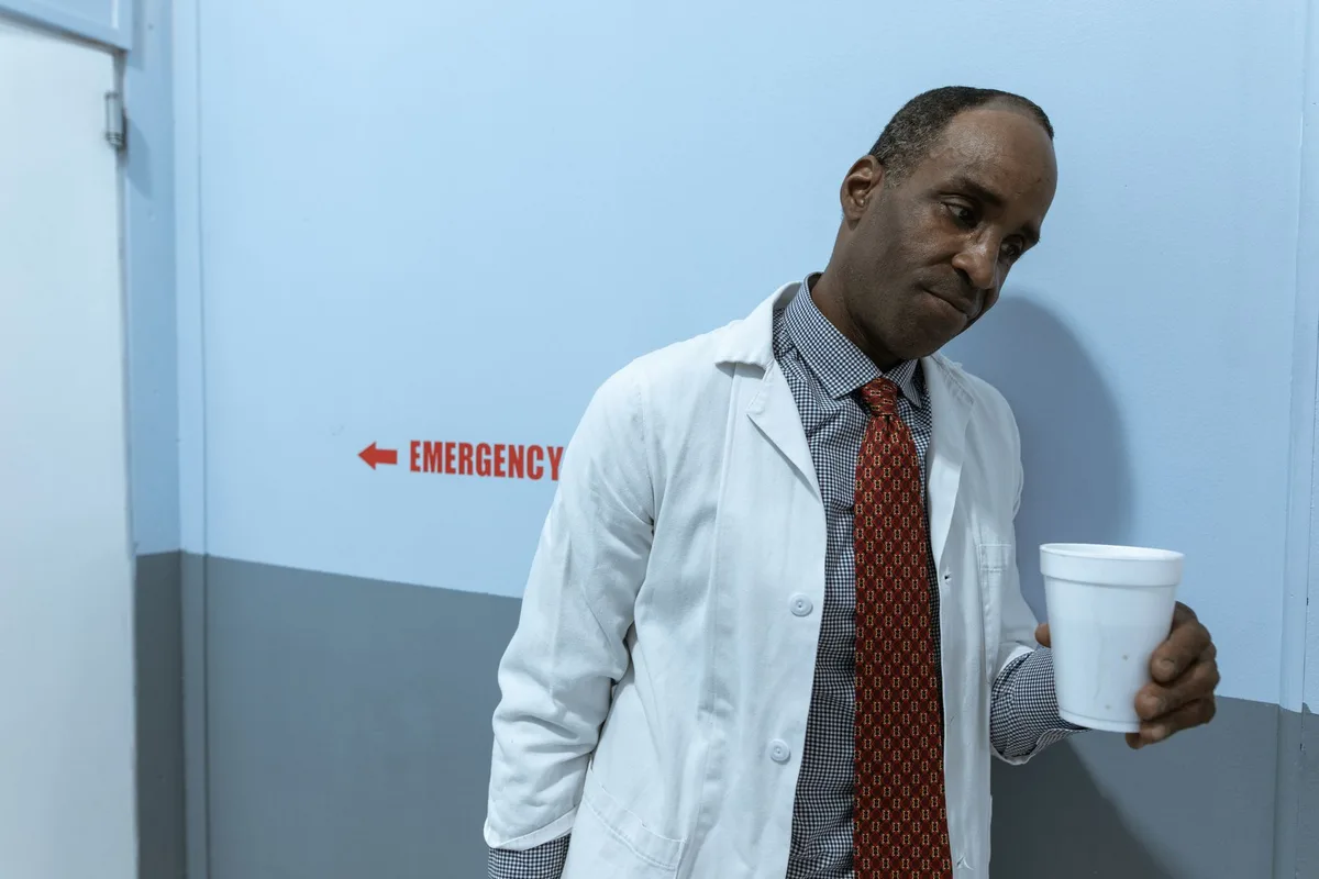 A woman in professional medical attire standing in a modern hospital corridor, harsh lighting casting shadows on her face, an air of cold ambition and superiority