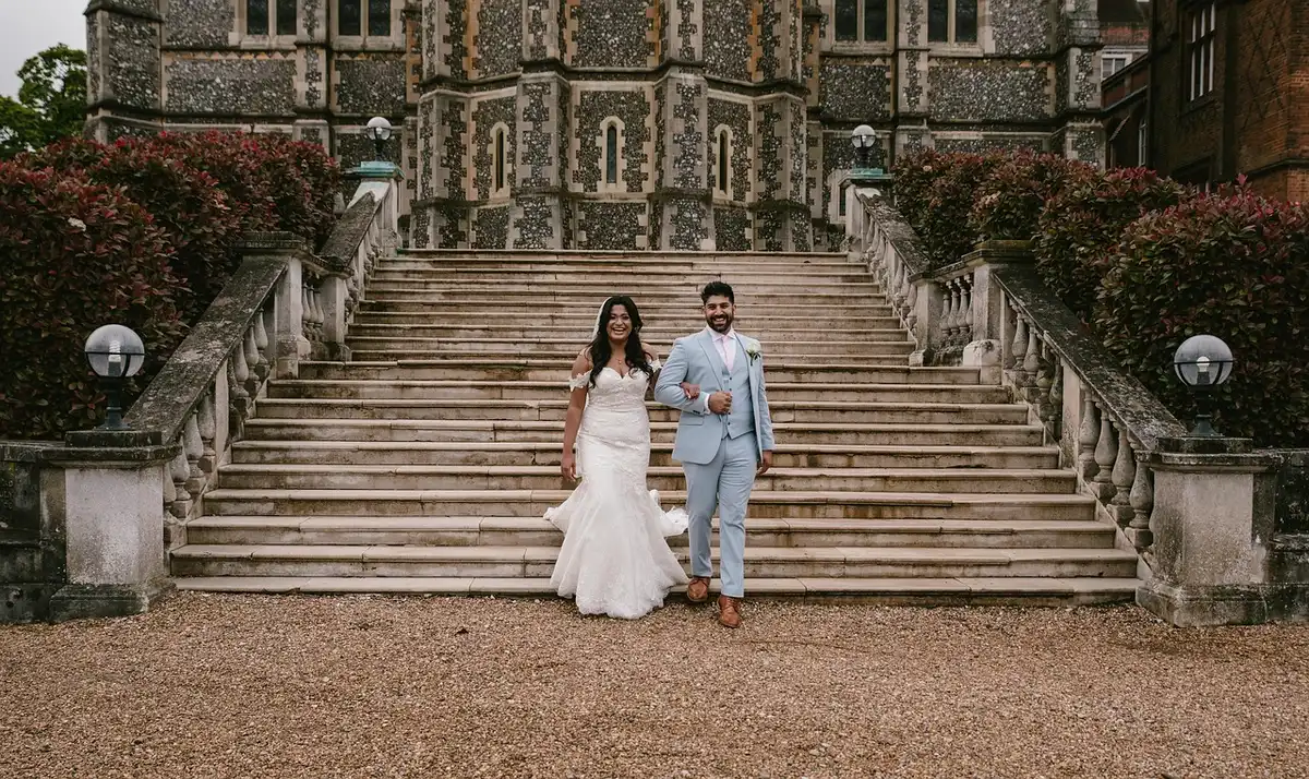 Bride in hand-embroidered white gown with crystal beadwork, standing in elegant mansion reception space with golden lighting and floral arrangements