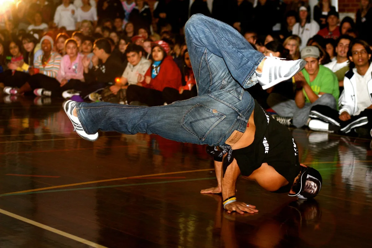 A competitive freestyle battle moment, three MCs on stage under intense spotlights, the crowd watching intently in a packed outdoor venue, tension and focus visible in the performers' expressions.