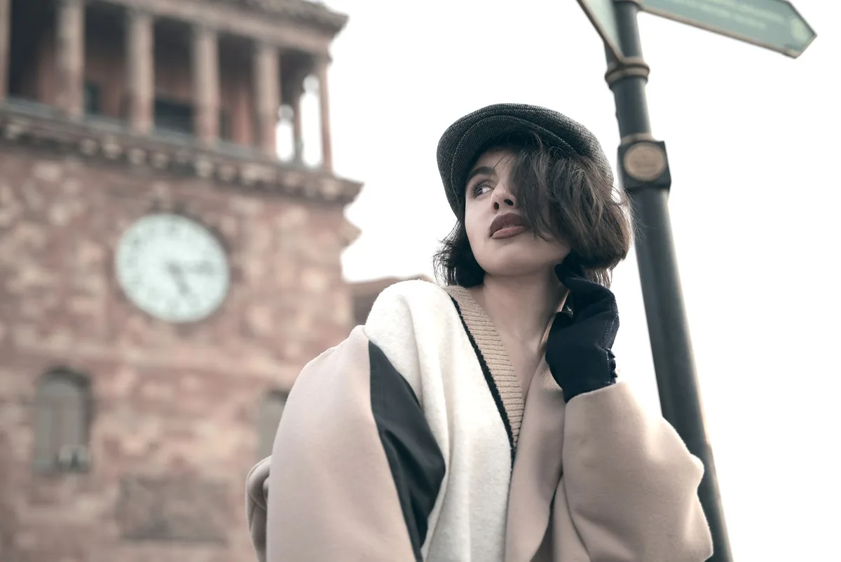 Elegant vintage-inspired outfit with high-necked pie-crust collar blouse, classic pillbox hat with bow accent, soft grey tweed jacket, and golden dangly earrings, worn by an anonymous woman arriving at a country church on a sunny day