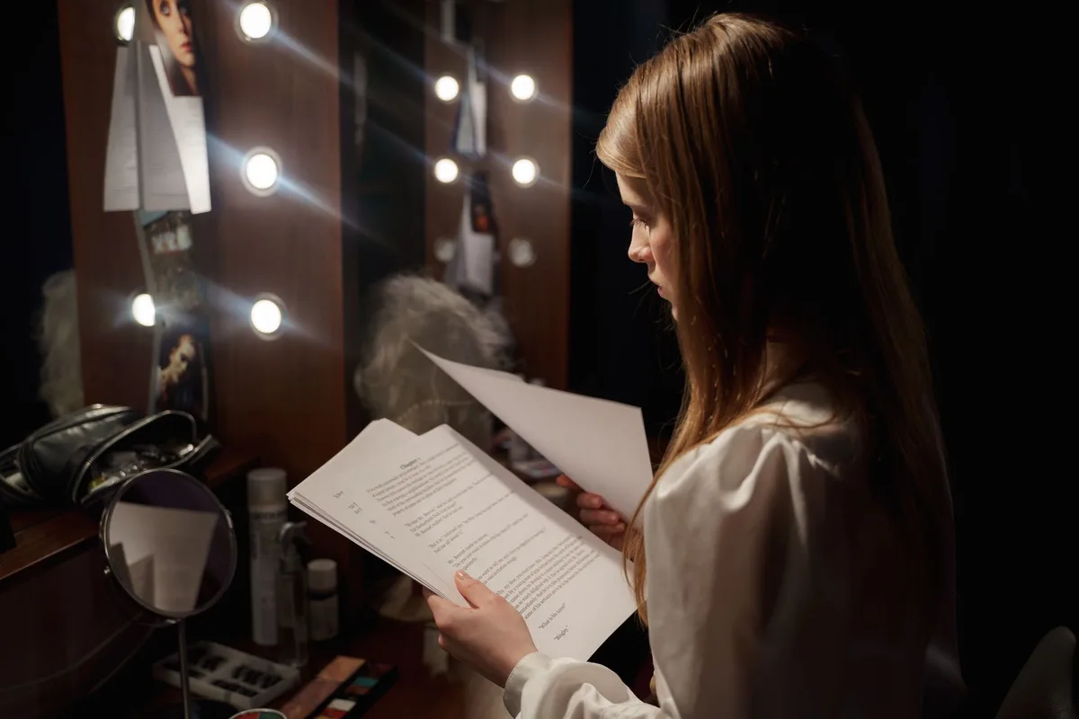Mulher de meia-idade em estúdio de televisão, com iluminação profissional, olhando para câmera com determinação e sabedoria, refletindo décadas de experiência artística