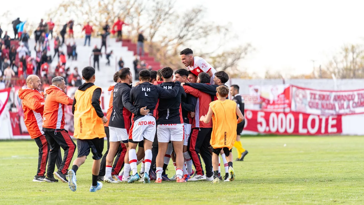 A stadium crowd erupting in celebration, arms raised and scarves aloft, anonymous fans in motion under floodlights, the energy of a historic moment.