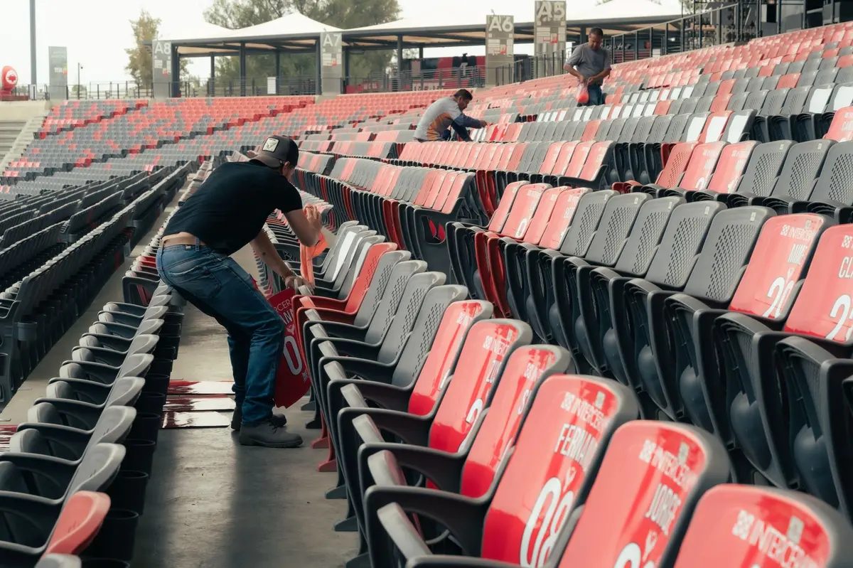 An empty stadium seat in dim light, goal post in the background slightly blurred, the silence of defeat.