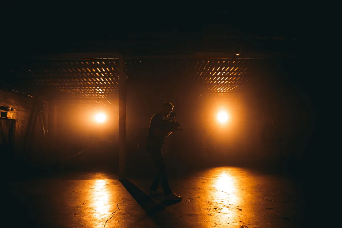 An empty film set with dramatic lighting, a lone actor's chair center-frame, production equipment blurred in shadow, anticipation in the atmosphere