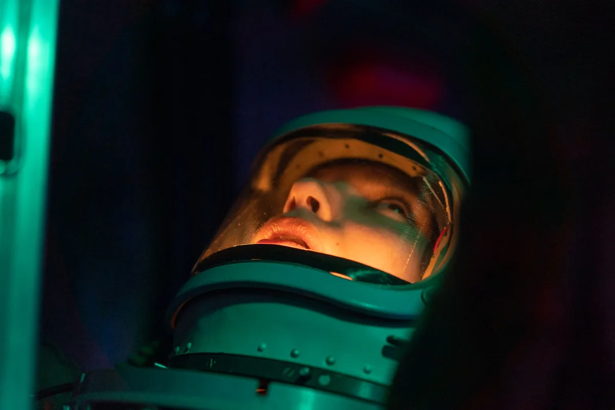A futuristic spaceship interior with glowing neon panels and control screens, a lone pilot seat facing a starfield through a viewport, cosmic dust drifting in light