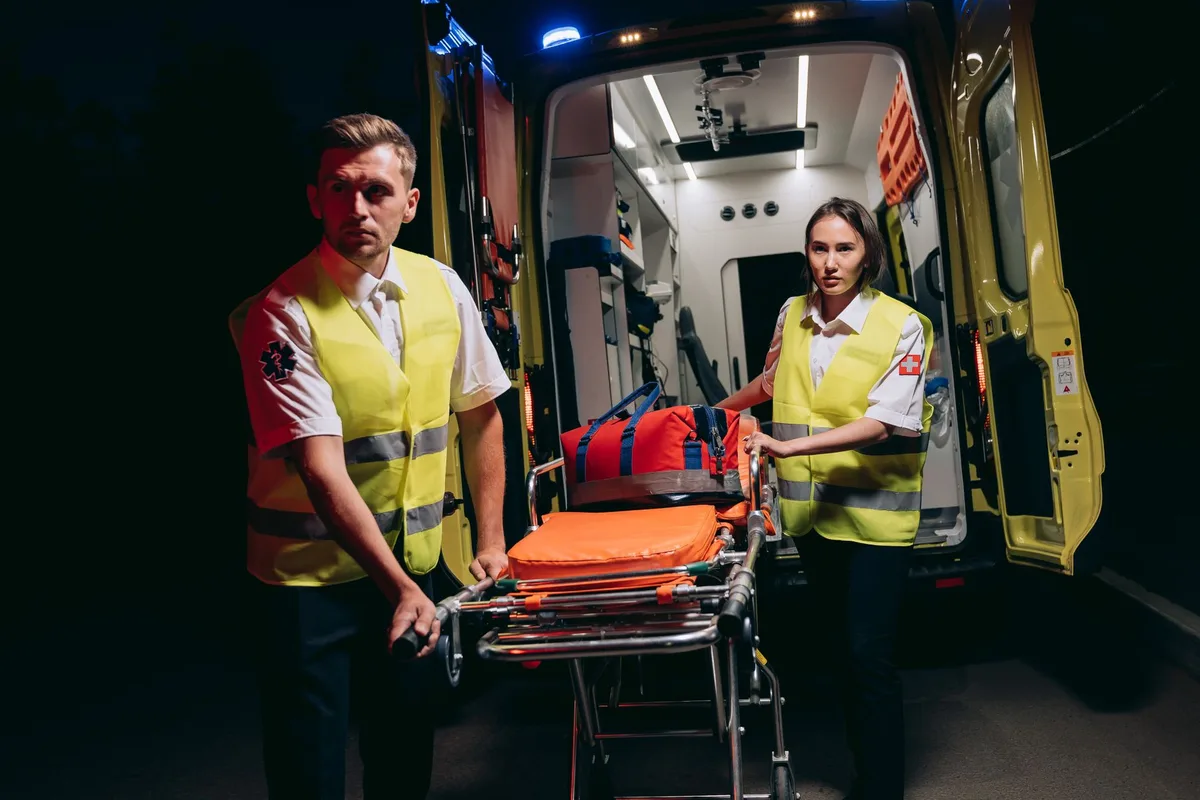 A mobile emergency unit parked on an urban street, paramedics in uniform preparing equipment, the night sky above, focused intensity on their faces.