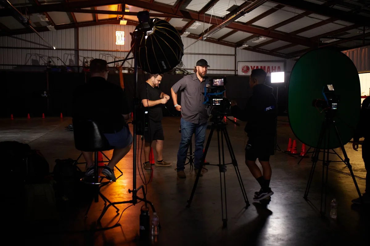 Early evening TV studio setup with professional lighting rigs, a formal interview stage with two empty anchor chairs facing a single guest seat, the Globo logo subtly visible, studio audience silhouettes in soft focus, ready for live broadcast.