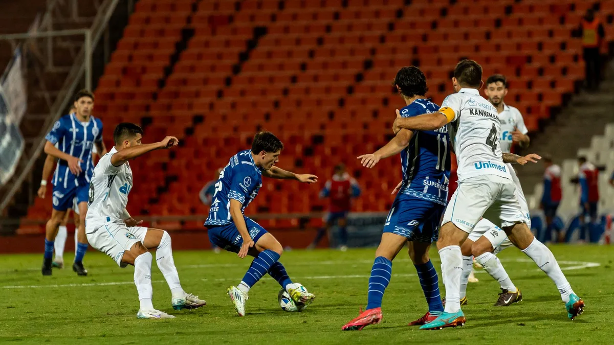 Premier League match action scene with anonymous players in motion, ball mid-air, stadium crowd blurred in background, evening light across the pitch