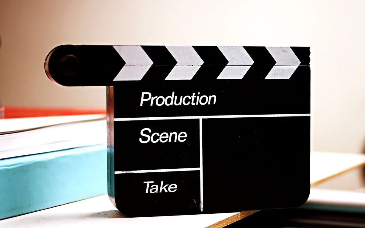 A film clapperboard resting on a wooden table in a dim studio, with production notes partially visible, soft overhead lighting casting shadows, suggesting a paused or abandoned shoot.