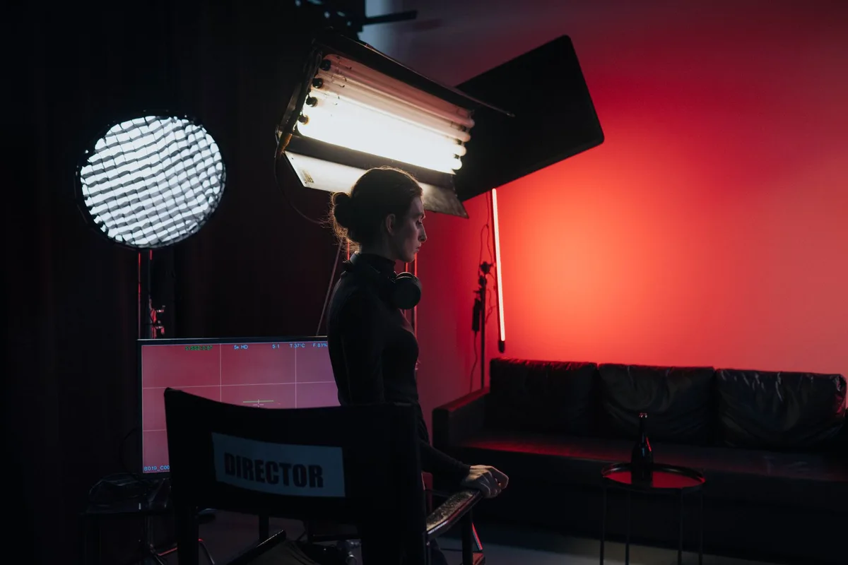An abandoned film set with camera equipment and lights in a dark warehouse, a single spotlight illuminating an empty chair, production halted mid-shoot