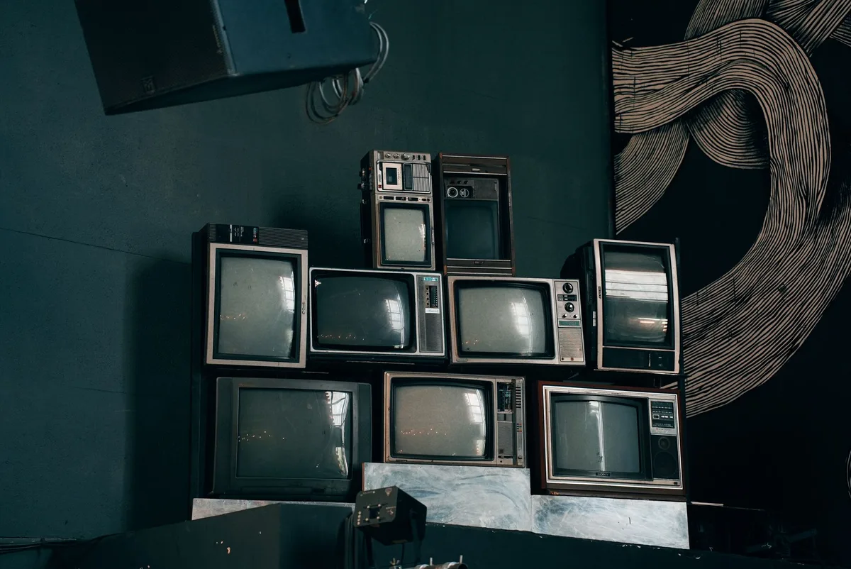 A vintage television set from the 1950s on a studio set, warm lighting casting long shadows, with broadcast equipment visible in soft focus behind it, capturing the era of early television