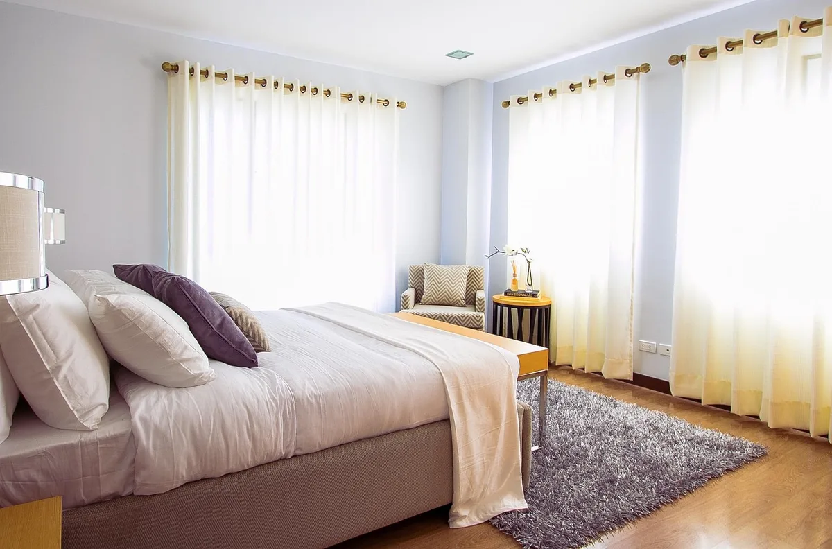 A dimly lit apartment interior with a single window, early morning light filtering through curtains, a solitary armchair in shadow, the scene evoking an empty, quiet moment