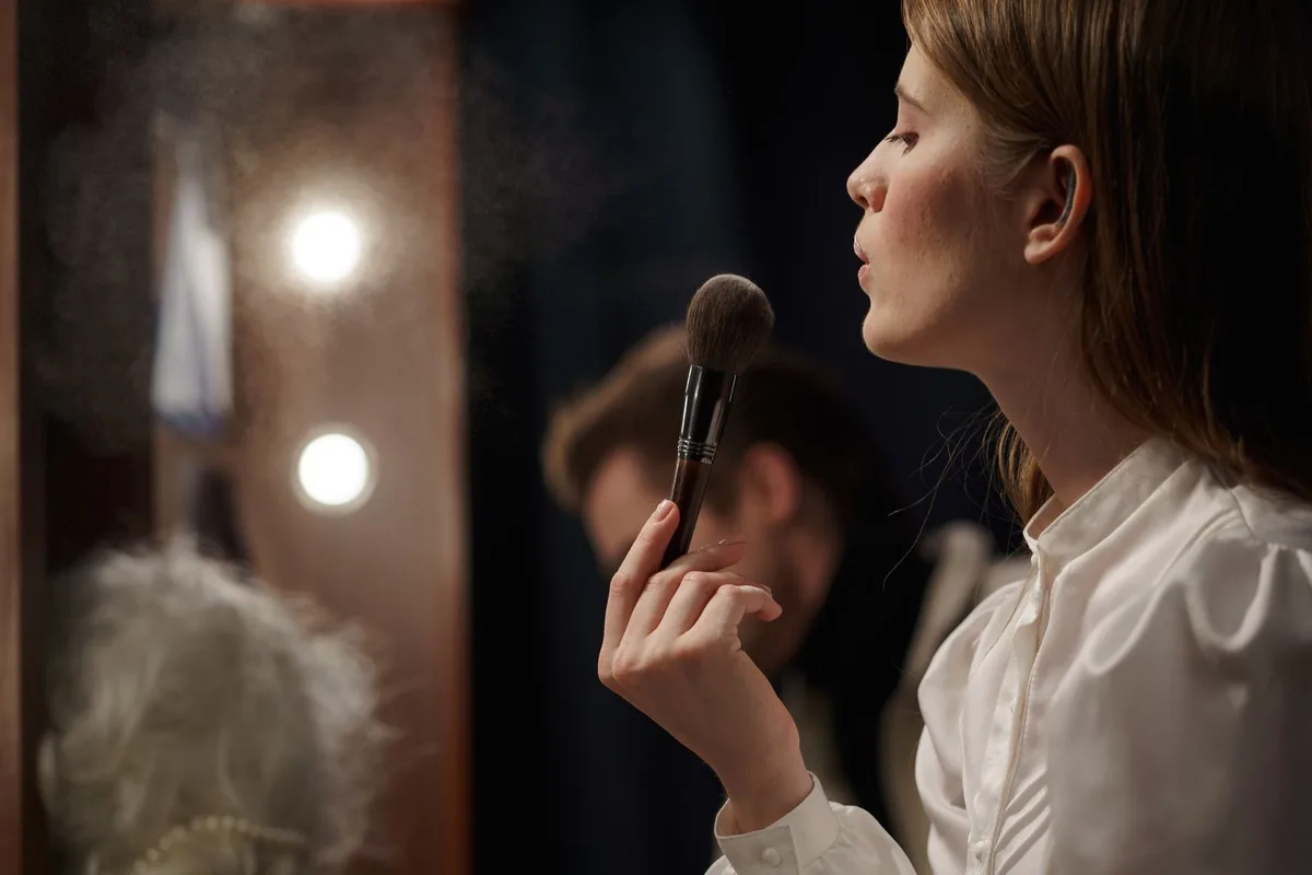 Actress on stage during live TV broadcast, phone in hand, caught mid-text, studio lights bright, playful expression, moment of surprise