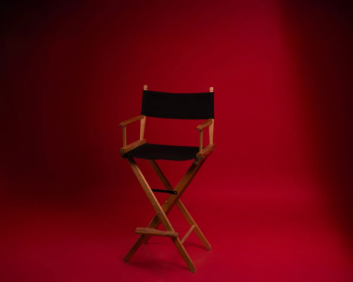 An empty theater stage under soft spotlight, a single director's chair center-stage, worn scripts scattered on the wooden floor, theatrical curtains in shadow behind, intimate and contemplative