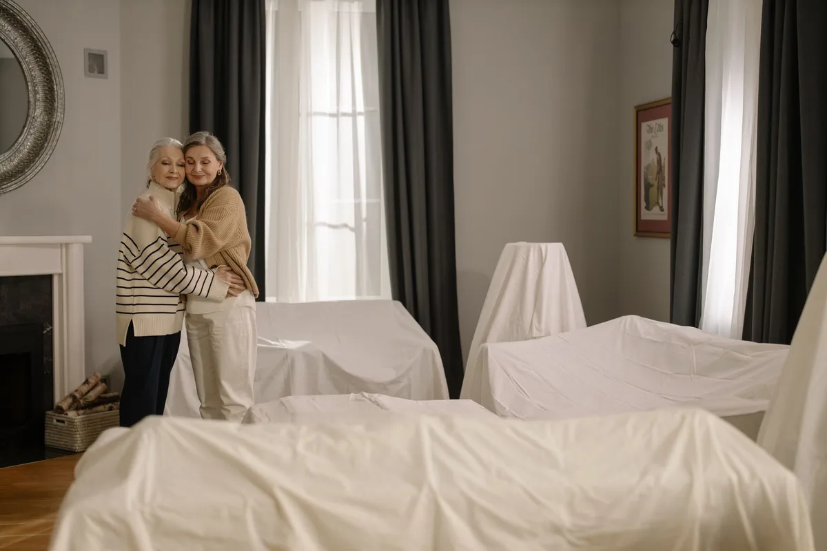 An intimate family moment, two women laughing together in a sunlit room, one elderly with silver hair, the other younger, sharing warmth and connection, embodying decades of genuine affection.