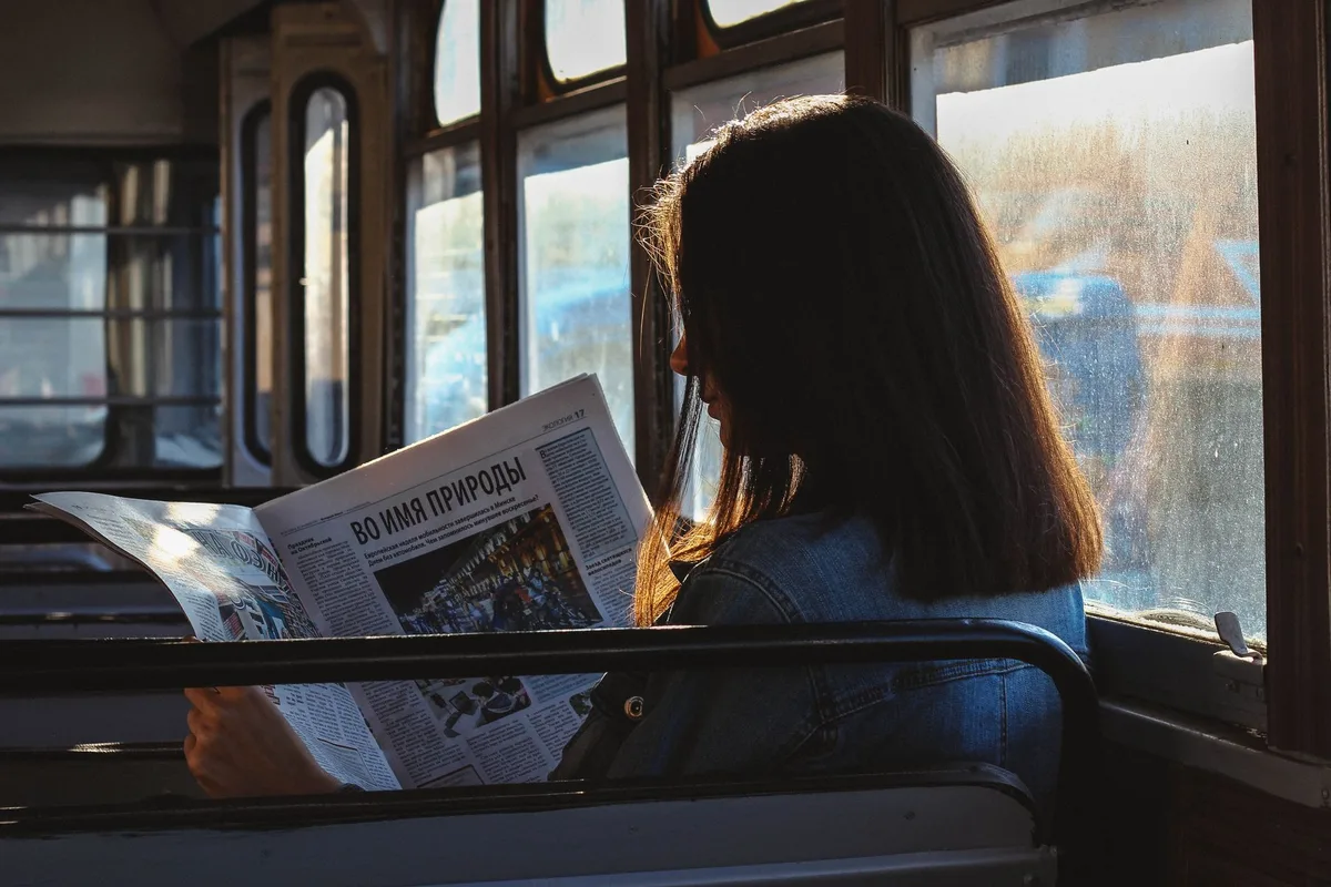 A newspaper with bold headlines visible, candlelit period room, sense of danger and exposure, shadows falling across the page