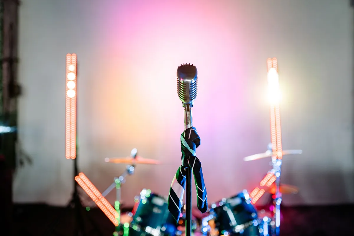 A concert stage with a single microphone stand under dramatic lighting, an empty auditorium behind it, symbolizing the voice and platform, with subtle feminist symbolism in the composition.