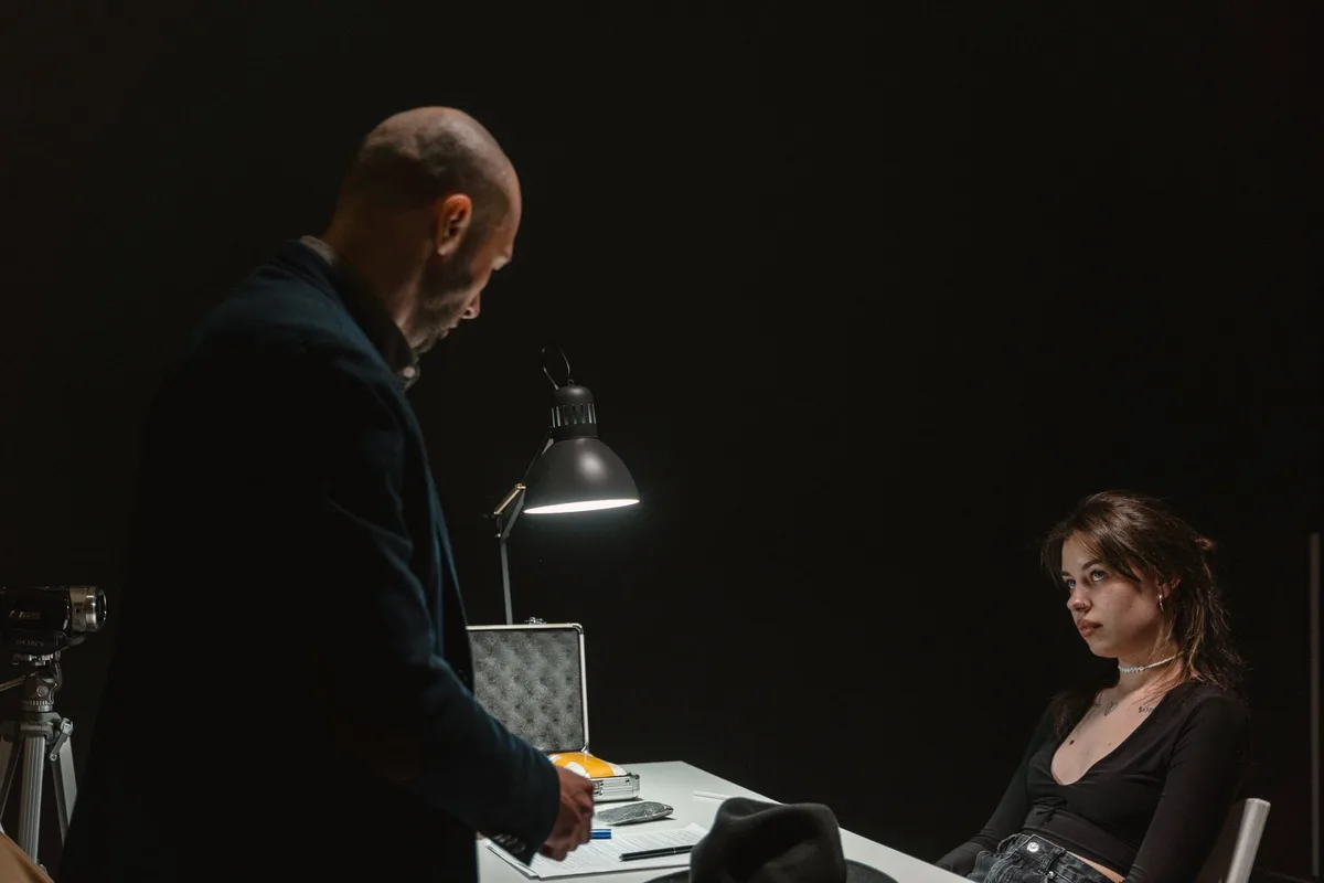 A dimly lit television studio set with a single spotlight illuminating an empty director's chair, suggesting dramatic tension and complex character work in a crime thriller production.