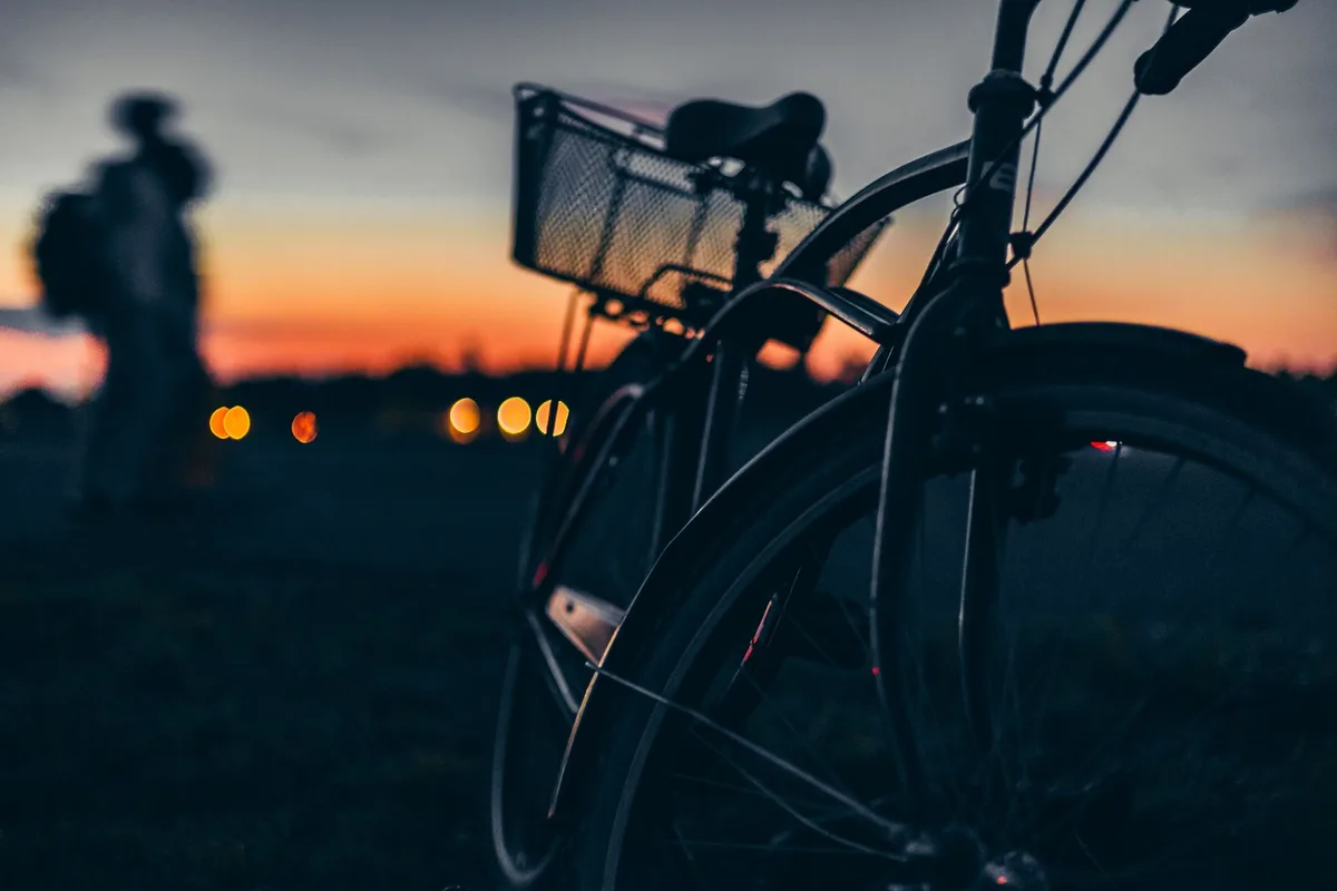 A cyclist in motion on a tree-lined rural road in Maine, pedaling through golden afternoon light, with the road stretching toward distant hills.
