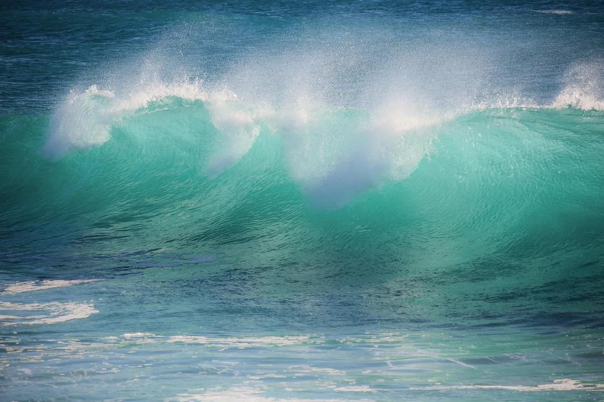 A team of two surfers riding a massive wave in tow-in format, with jet-ski assistance visible, ocean spray and power visible in the moment.