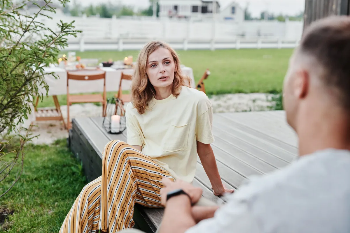 Two people sitting at a table having a calm conversation, facing each other with attentive expressions, warm lighting suggesting intimacy and mutual respect, no identifiable faces visible