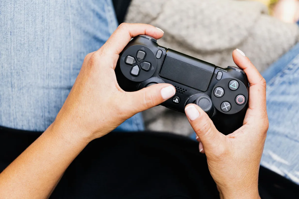 A gamer's hands on a controller with a faint glow from a television screen in the background, showing the moment of experiencing enhanced graphics during gameplay.