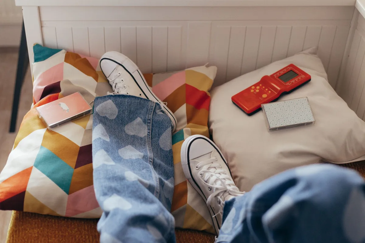 An empty summer bedroom with afternoon light streaming through windows, a single bed neatly made, posters of musicals on walls, a stack of books and DVDs on a nightstand, sunlight casting long shadows, intimate and quiet atmosphere