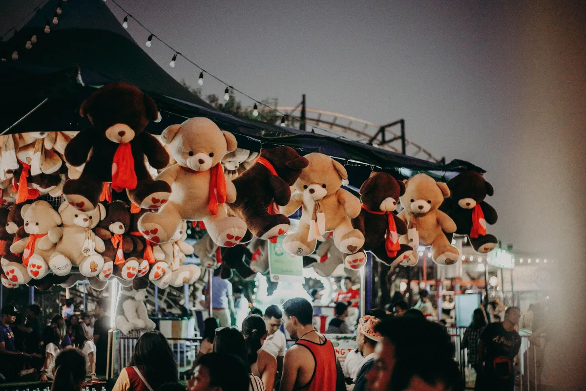 Crowded festival camping area at dusk with string lights overhead, anonymous families and couples enjoying the atmosphere, festive energy visible in body language and movement