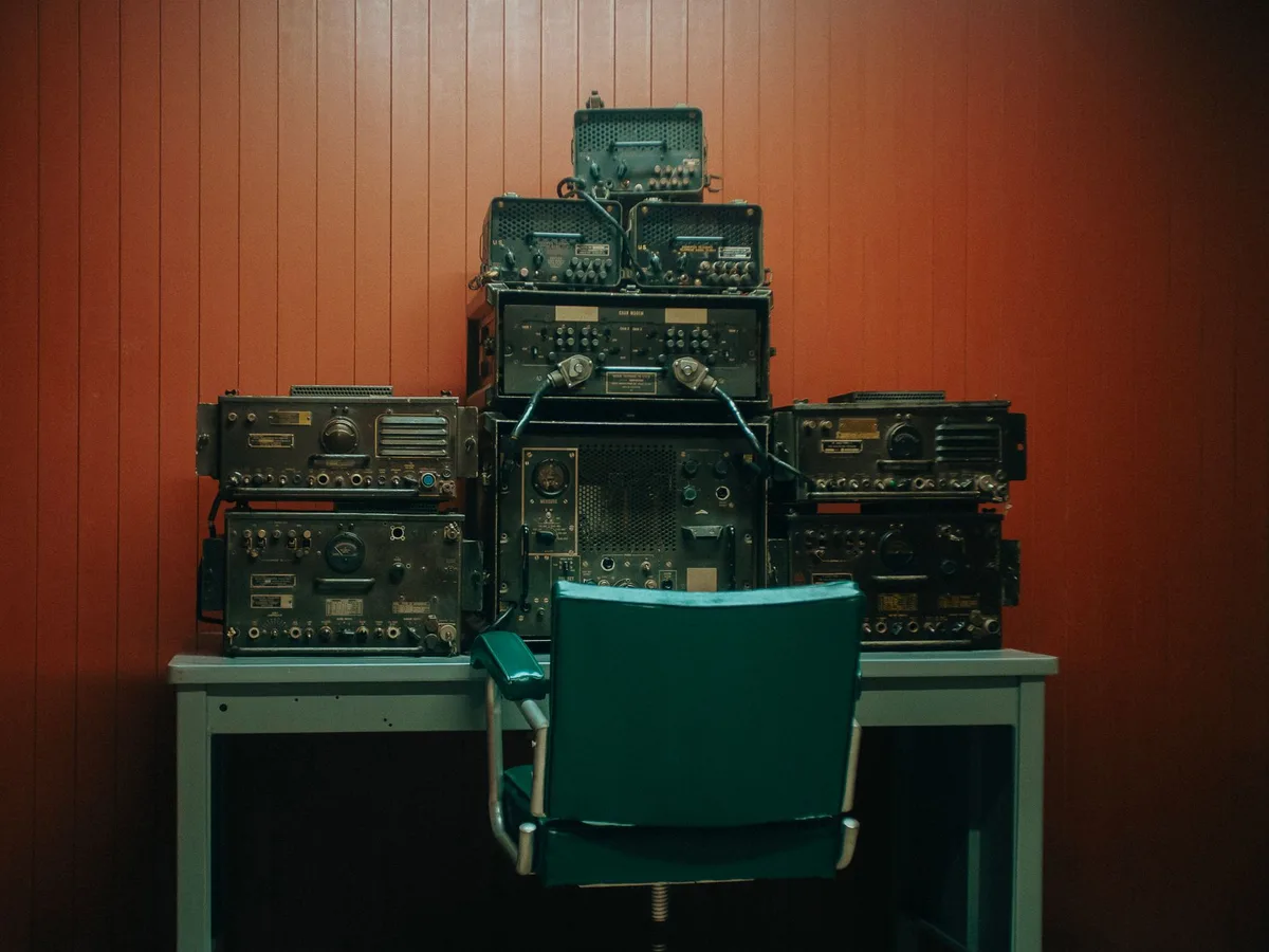 A figure sitting in a dimly lit control room, silhouetted against glowing monitors displaying game footage, hands resting on a mixing console, the scene conveying anticipation and focus.
