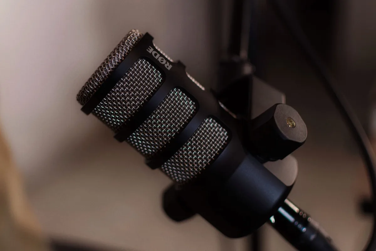 A spotlight illuminates a microphone on a broadcast studio stand, with blurred stadium lights and crowd silhouettes in the background, capturing the energy of live sports commentary.