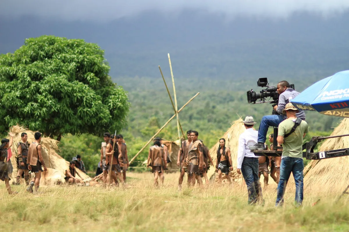 Bastidores de gravação de novela, atriz em maquiagem, equipe ao fundo desfocada, refletindo o dia de trabalho