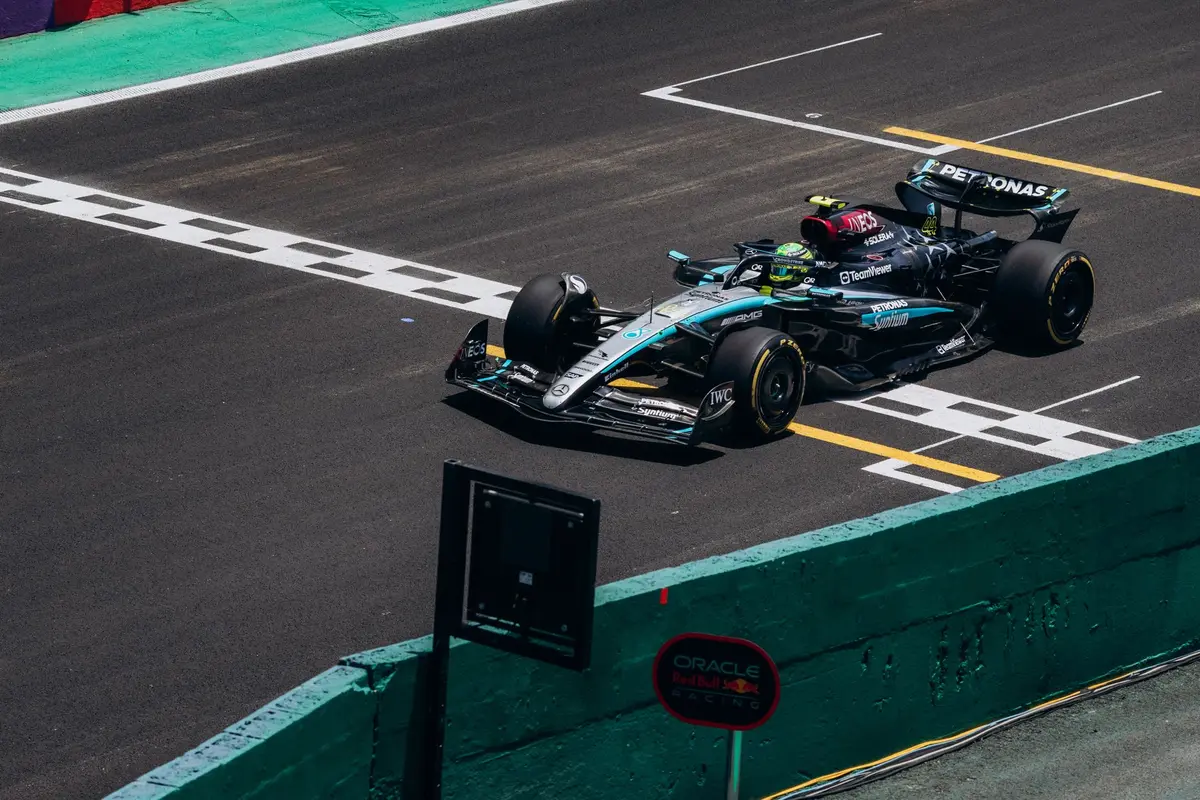 A British racing driver in silver Mercedes gear celebrating a sprint victory on a podium, arms raised, confetti falling, crowd silhouettes blurred in background, pure elation visible