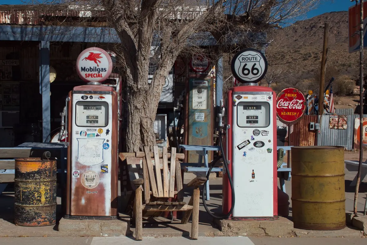 A vintage 1960s diner or street scene with retro cars and period-accurate storefronts, bathed in warm afternoon light, suggesting a time-travel narrative