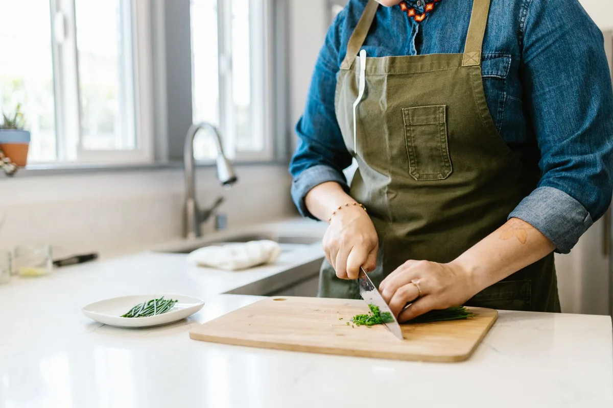 A person at a kitchen counter surrounded by fresh ingredients, thoughtful expression, ambient kitchen lighting showing quality produce and cooking tools, representing personal culinary journey and learning