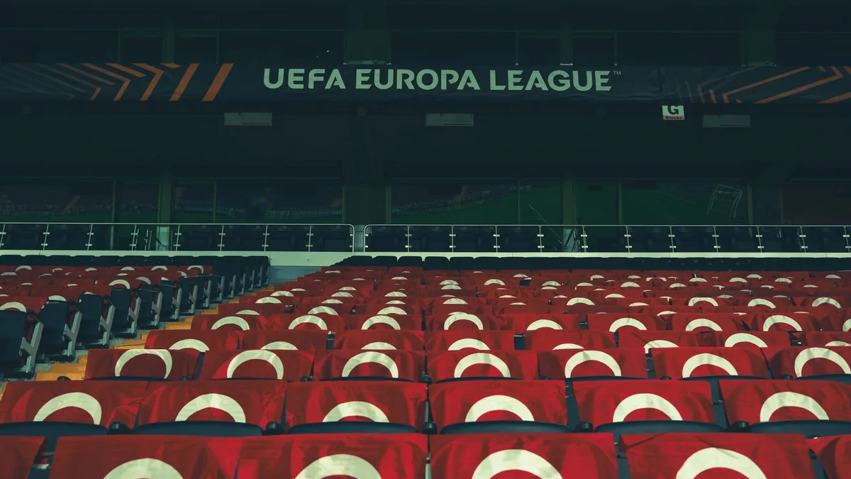 An empty stadium corridor dimly lit, a single locker room door ajar, tactical board visible in soft focus, the atmosphere after a defeat