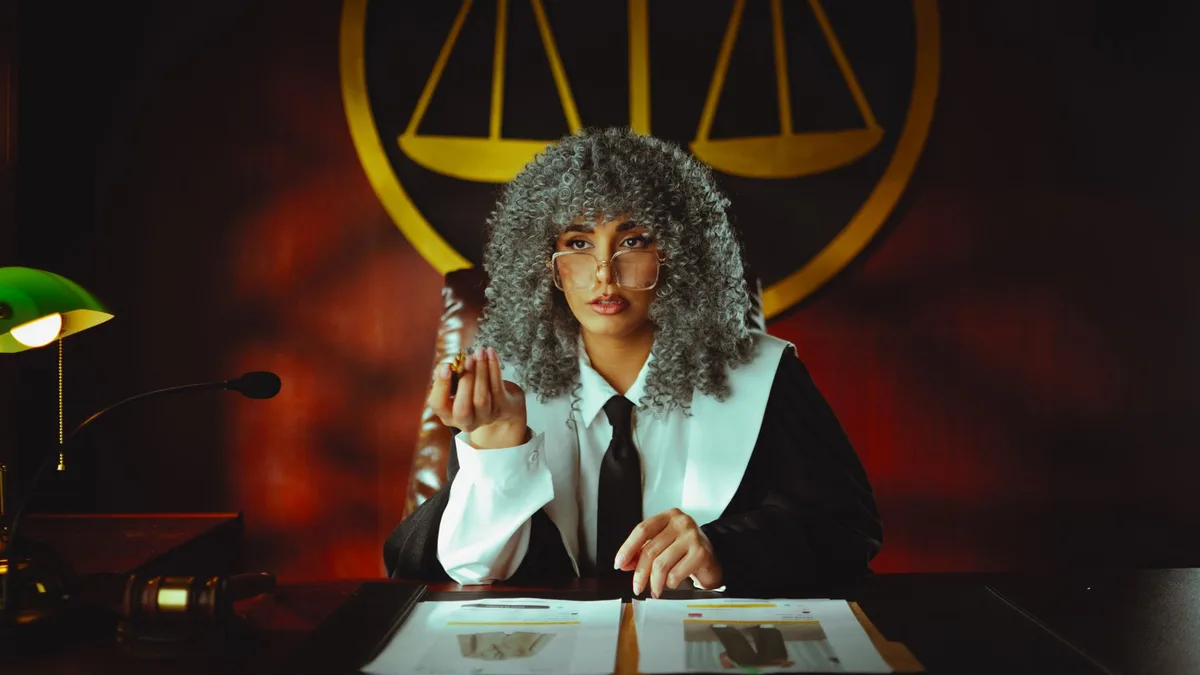 A state prosecutor sits in a dimly lit office, papers scattered on desk, a single lamp casting harsh shadows, conflict evident in her posture as she contemplates a difficult choice between duty and family loyalty