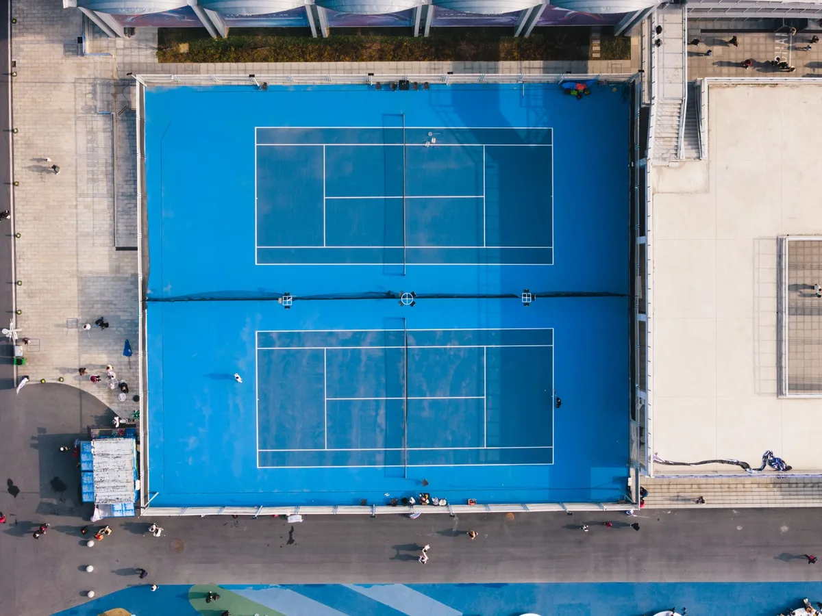 Professional tennis court with qualifying round setup, empty seats in the stadium, and pristine white court lines under bright floodlights