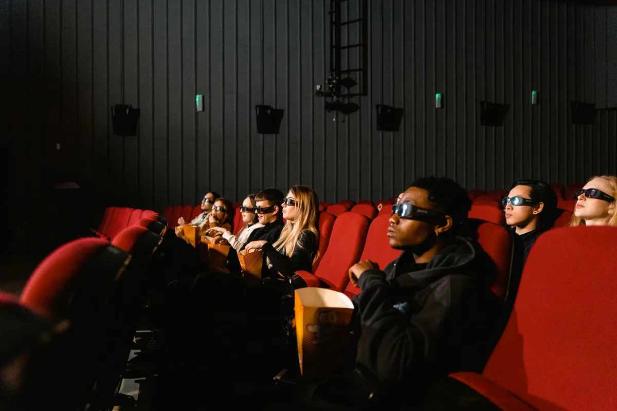 Modern cinema theater with premium large-format screen, dramatic lighting from the projection, empty rows of seats, and sleek technological setup.
