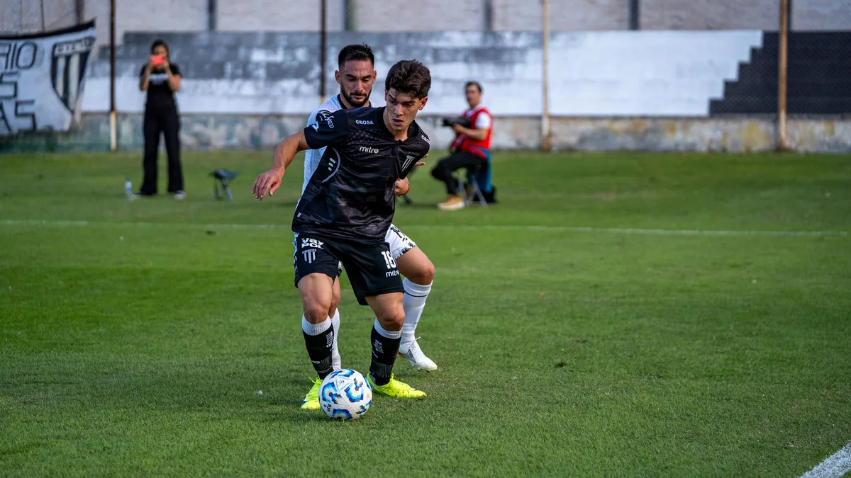 Vinicius Jr em ação no campo, driblando um defensor com a bola sob controle, em uniforme branco do Real Madrid, com torcida ao fundo desfocada