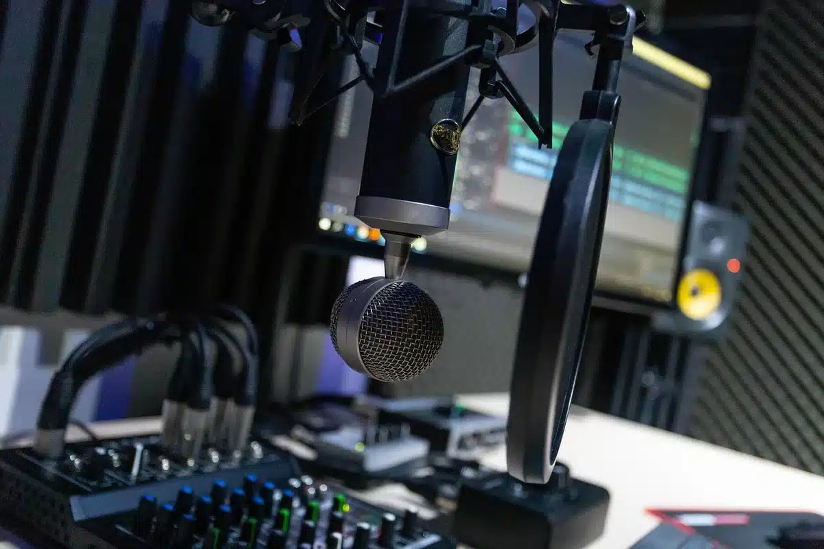 A broadcast studio microphone under studio lighting, with empty chairs and control panels in soft focus behind it, representing a presenter's absence from the airwaves.
