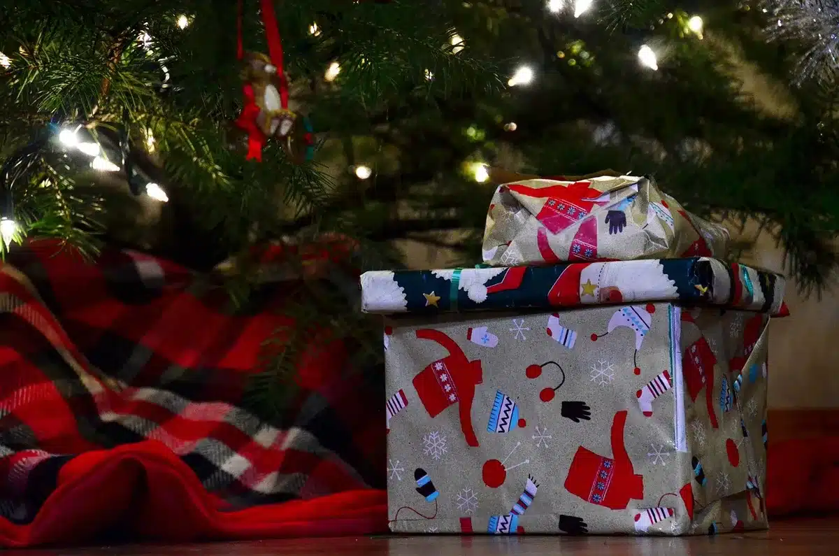 A festive winter scene with wrapped presents scattered across snowy ground, a glowing magic bag in the center emitting golden light, twinkling holiday lights in soft focus background