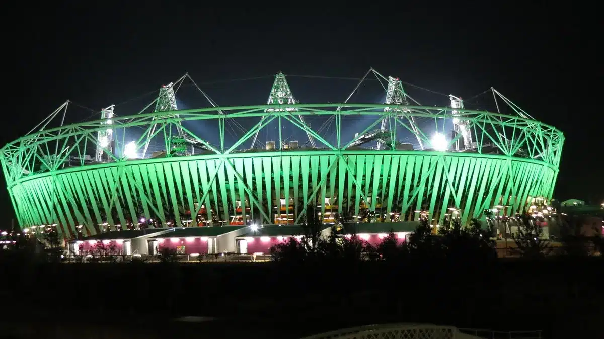 Empty Emirates Stadium seats bathed in red light, a single raised fist silhouette against the glow, confetti suspended mid-air, jubilant crowd blur in motion