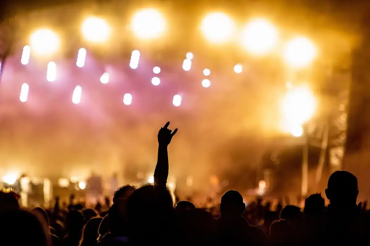 Palco Mundo do Rock in Rio com luzes de palco iluminando uma multidão dançante, braços levantados, mosh pits em formação, energia vibrante de um show de metal contemporâneo