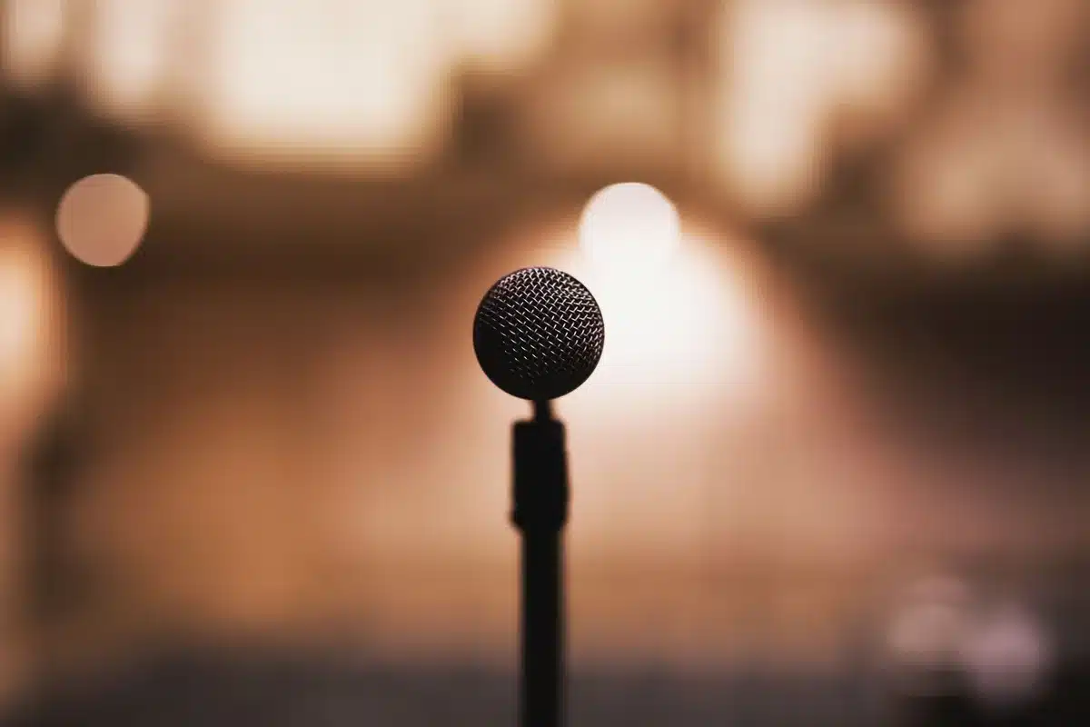 Empty stage with a single microphone under a spotlight, dust motes in the beam, an abandoned set of headphones on the floor hinting at a singer's arrival