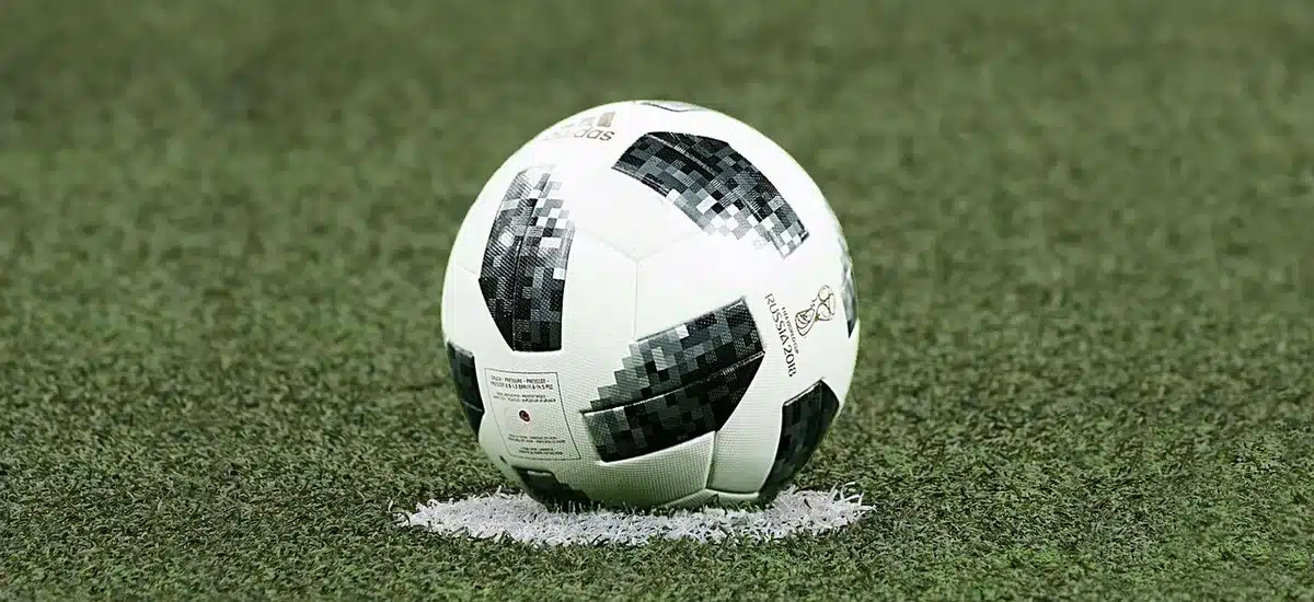 Close-up of an empty football pitch under floodlights, a lone corner flag and empty stands in soft focus