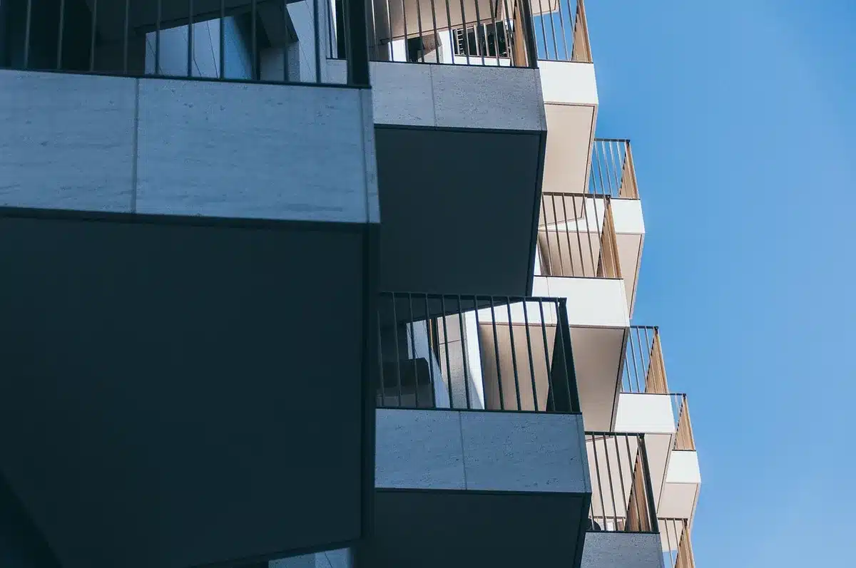 A brutalist concrete office building with geometric relief panels, situated in a historic city center with castle ruins visible behind it, showing architectural contrast
