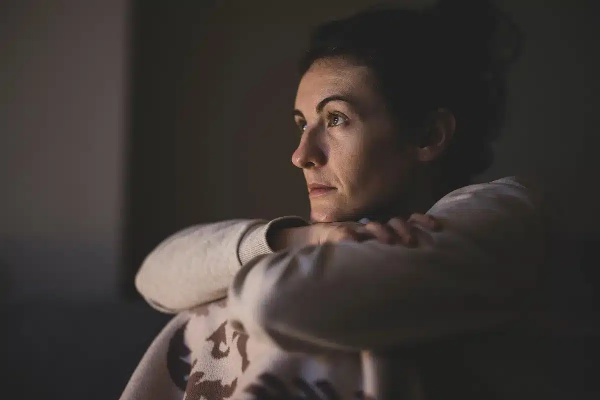 anonymous person sitting in dark living room watching a glowing TV screen, hands clasped, tense posture