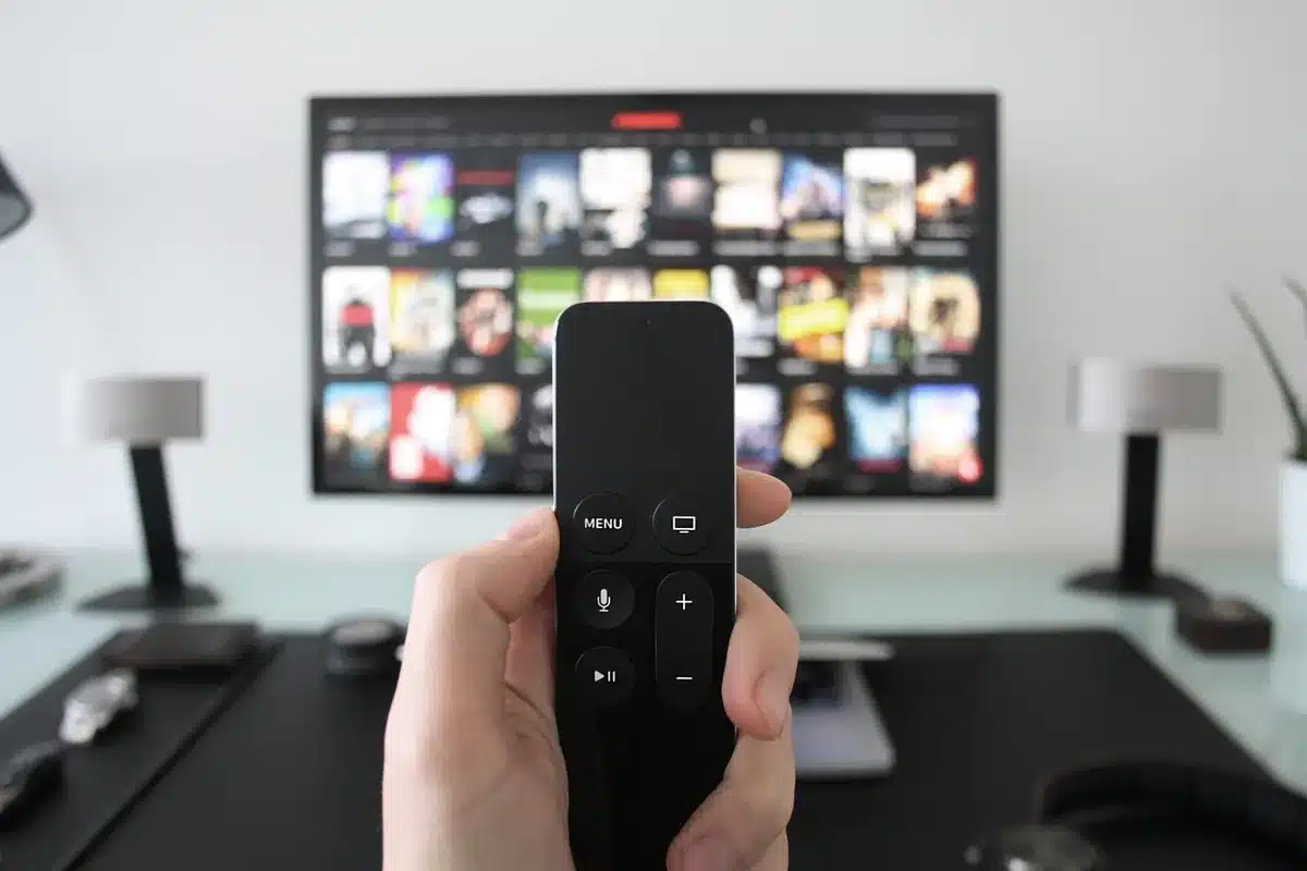 Close-up of a remote control on a sofa armrest and a dim TV screen showing a streaming menu