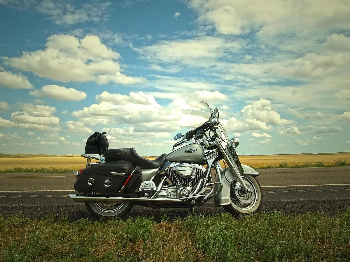 Empty rural road at dusk with a lone motorcycle parked by the roadside, distant oil pump silhouettes, moody sky