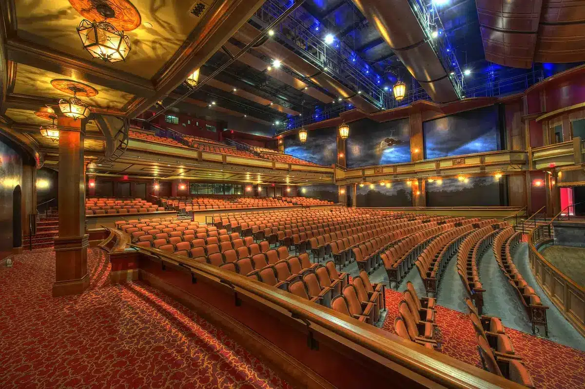 An empty concert venue with stage lights dimmed, a single spotlight illuminating an empty stage, rows of seats in shadow, quiet atmosphere of loss